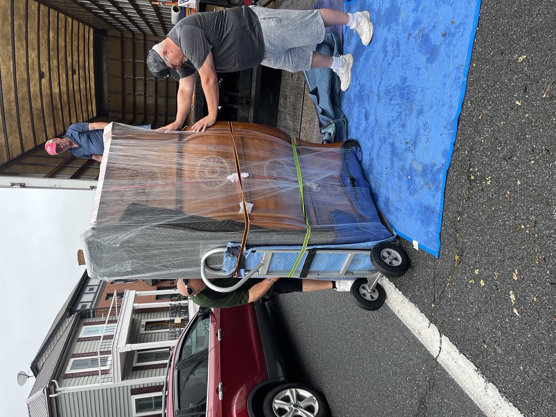 Wrapped furniture loaded carefully on a moving dolly outside a home